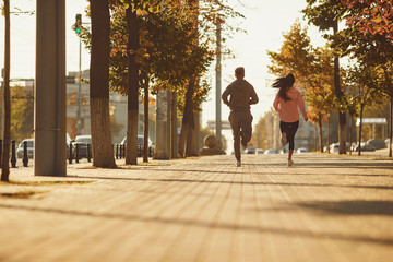 A man and a woman are running along the city street in the morning.