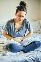 	
Woman suffering from abdominal pain while sitting on bed.