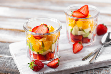 Concept of healthy food, clean eating. Low calories colorful sweet summer dessert. Homemade simple fruit salad, ideal breakfast. Orange, apple, strawberry. White wooden background, closeup, macro 
