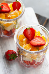 Concept of healthy food, clean eating. Low calories colorful sweet summer dessert. Homemade simple fruit salad in two glasses, ideal breakfast. Orange, apple, strawberry. White wooden background. 