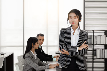 Young operator asian woman customer service agent with headsets standing with confidence in a call center office.  Professional workers working well in a team.
