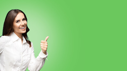 Portrait of happy smiling young excited businesswoman, showing thumb up hand sign gesture. Success in business concept studio shot. Over green color background.