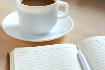 A cup of morning coffee and a notebook with a pen on the table. Business and Management