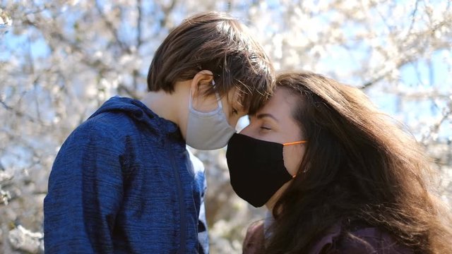 A mother with her son in masked shields stand near a blossomed tree in a spring park during the Kovid-19 epidemic.