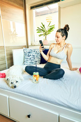 Cute girl relaxing after gym with dog while using cellphone.