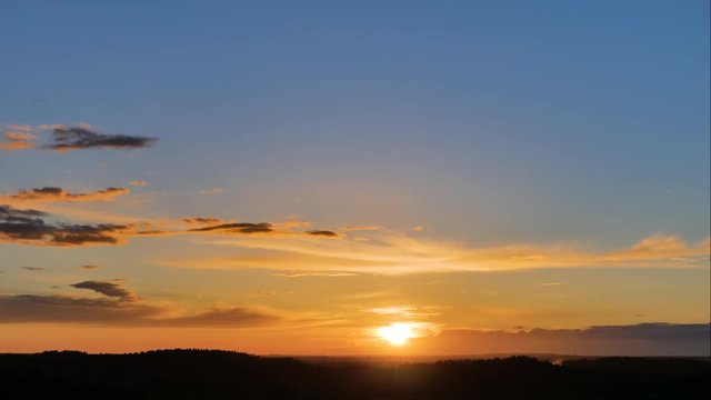 Aerial panoramic time lapse of a epic, picturesque and colorful sunset in orange and yellow tones on a blue sky with running clouds over a summer forest on the horizon. View from the hill in 4k