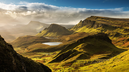 Scenic view of Quiraing mountains in Isle of Skye, Scottish highlands, United Kingdom. Sunrise time with colourful an rayini clouds in background. - obrazy, fototapety, plakaty