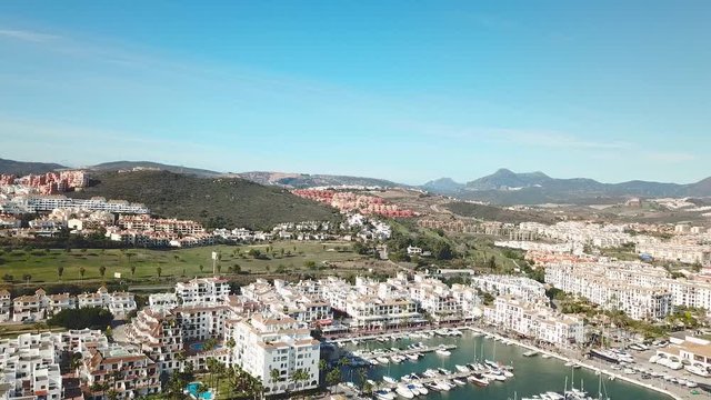 Aerial panoramic view of beautiful "Puerto de la Duquesa" in MANILVA- Malaga SPAIN. Yachts and boats docked in the Harbour. Luxury Apartment Urbanisation and Restaurants . Drone going backward.