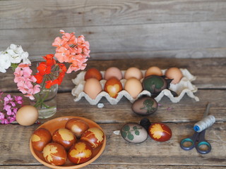 Getting ready for Easter.We tie the eggs with a net with leaves and paint the onion peel. Pelargonium flowers in a glass, on a natural wooden old background.