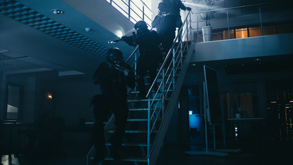 Masked Squad of Armed SWAT Police Officers Run Down the Stairs from a Second Floor in a Dark Office Building. Soldiers with Rifles and Flashlights Move Forwards and Cover Surroundings.