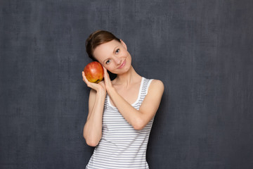 Portrait of happy young woman holding ripe apple in hands and smiling