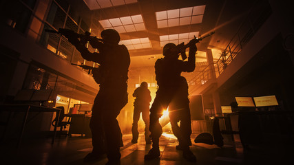 Masked Squad of Armed SWAT Police Officers Move in a Hall of a Dark Seized Office Building with Desks and Computers. Soldiers with Rifles Surveil and Cover Surroundings. Warm Color Grading.