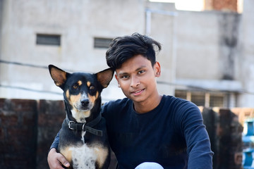 a teenager boy with his black indian dog portrait looking to the camera outdoor