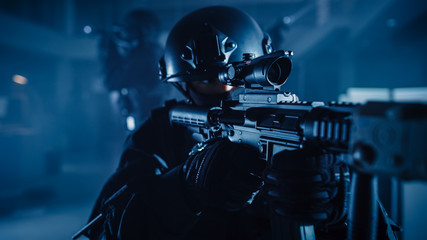 Close Up Portrait of Masked Squad Member of Armed SWAT Police Officers Who Storm a Dark Seized Office Building with Desks and Computers. Soldiers with Rifles and Flashlights. 