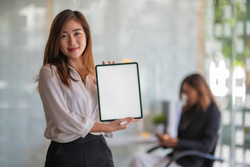 Portrait of young beautiful business woman showing blank screen digital tablet while standing in office room
