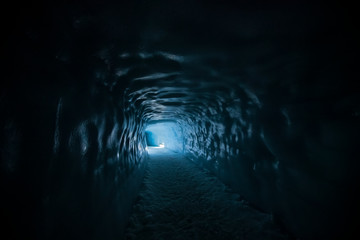 Blue Light at the end of a tunnel. Beautiful textured ice walls are visible in an ice cave inside a...