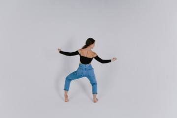 Stylish beautiful dancer wearing black leotard with open shoulders and blue jeans dancing on the white backgroud