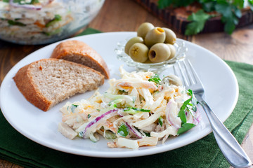 Layered salad with mayonnaise, garnished with olives and parsley, selective focus