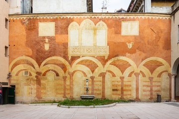 The architecture of the old part of the city of Verona in Italy. Decorative fountain in front of a wall-painted building.