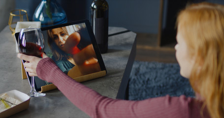 Attractive mid-30s Caucasian female clinking glasses while chatting with a friend or partner online in video chat, using a tablet
