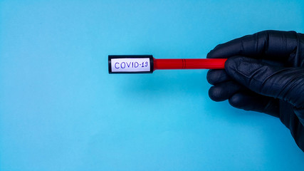 Coronavirus Covid-19 Vacuum Tubes For Medical Work With Blood Samples In The Laboratory. Coronavirus Test. A doctor's hand in a black rubber medical glove. Space for text on a blue background.