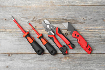 Hand-held construction tools electrician's screwdrivers, wire cutting and Stripping shears, and a knife on a gray wooden table. Electrician and installer tools on the table