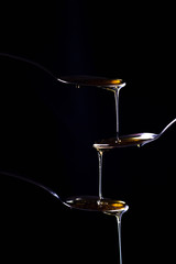 Three spoons on a black background, one above the other. Honey trickles down from the top of a...