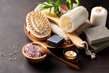 Spa. The concept of the bathroom. Natural cosmetics for the body and face. Sea salt, soaps of herbs and dead sea mud, loofah washcloth, massage brush on a dark table.