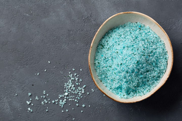Home Spa. Blue sea salt with seaweed for the body in a bowl on a dark grey background. Top view. Space for text.