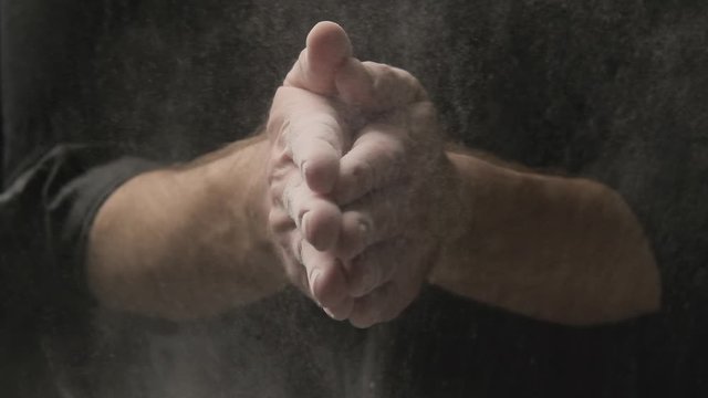 Baker clapping his hands filled with flour. Professional cook claps hands and powder fly. Baking concept. Flour cloud at black background