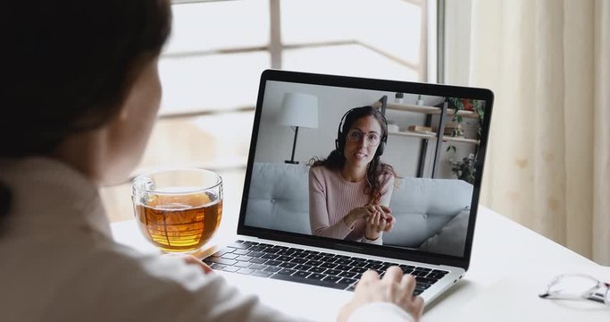 Happy young online teacher wears headset communicates with distant student gives web education class talks in webcam chat video conference call on laptop screen. Elearning concept. Over shoulder view