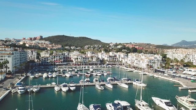 Aerial panoramic view of beautiful "Puerto de la Duquesa" in MANILVA- Malaga SPAIN. Yachts and boats docked in the Harbour. Luxury Apartment Urbanisation and Restaurants. Forward and right rotation.