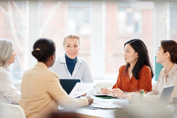 Portrait of diverse group of businesswomen discussing project while sitting at table during meeting in office, focus on smiling female boss