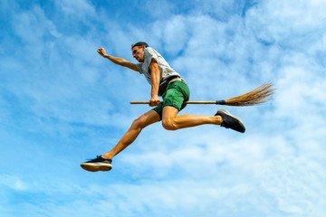 Young man flying on the broom with outstretched arm in the blue sky of Siquijor