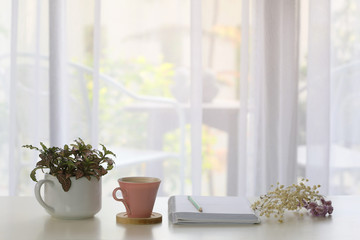 Fototapeta na wymiar Interior house decor with pink coffee and white notebook and blue pencil and plants with see through curtain 