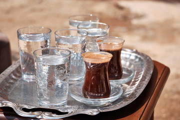 Glasses of water and Turkish coffee are on a metal tray