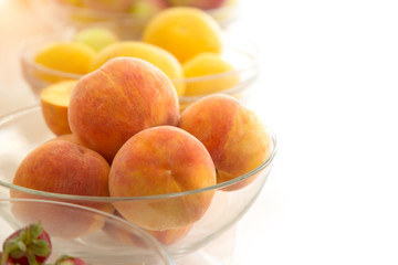 Yellow peaches in a glass dish on a white background. Copy space on right.