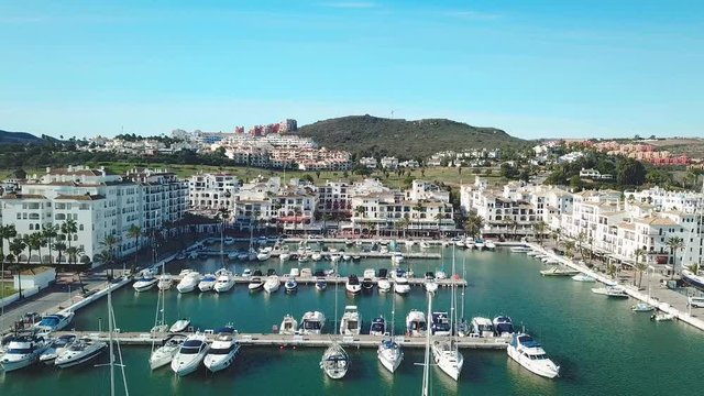 Aerial panoramic view of beautiful "Puerto de la Duquesa" in MANILVA- Malaga SPAIN. Yachts and boats docked in the Harbour. Luxury Apartment Urbanisation and Restaurants . Drone going backward.