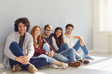 A group of friends is sitting on the floor in a room on a gray background.