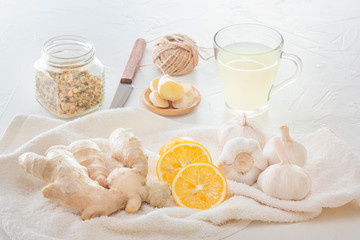Ginger, garlic, lemon, dried medical chamomile in a jar and ginger tea - a means to protect against viral infections and colds on a light wooden table.