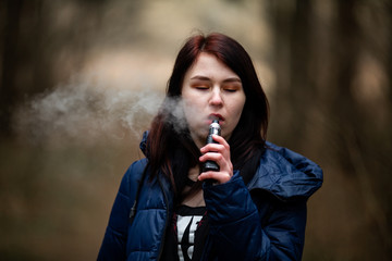 Vape teenager. Young pretty caucasian brunette girl smoking an electronic cigarette on the street...