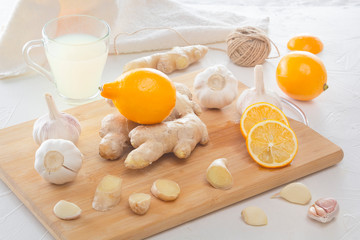 Ginger, garlic, lemon, dried medical chamomile in a jar and ginger tea - a means to protect against viral infections and colds on a light wooden table.