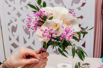 The florist's hands hold the bouquet of cream roses,orchid,ruskus leaves, pink gypsophila  in the...