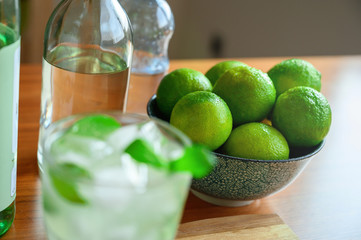 Refreshing alcoholic cocktail Mojito, white rum limes and soda mineral water on wooden board table background. Copy space. Bright summer drink, mint infused alcohol, ice cubes. Bottles in background
