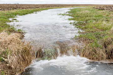 Motion blur of water flowing in farm field waterway to ditch after heavy rain and storms caused...
