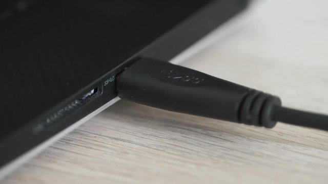 Hand Inserts USB Cable into Slot on Black Laptop, Carbon Fiber Surface - Macro Closeup