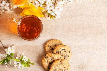 
Morning breakfast. Cup of tea , cookies with chocolate on the wooden background and spring flowers.
