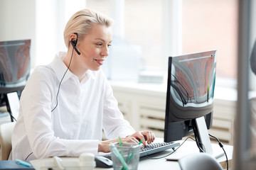 Side view portrait of female hotline operator using laptop and wearing headset while performing...