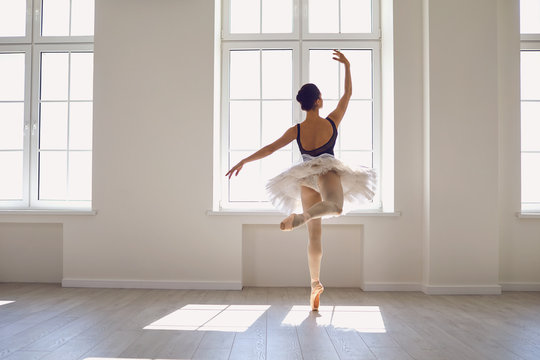 Fototapeta Ballerina. Young graceful ballet dancer is rehearsing a performance in a white studio with windows.