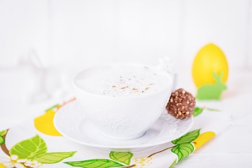 White porcelain cup of coffee cappuccino with cinnamon,chocolate candy and Easter decorations. Spring colors